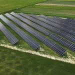 Widok z lotu ptaka na rozległą farmę fotowoltaiczną z panelami ustawionymi na terenie rolniczym, przeznaczoną do generowania energii słonecznej.