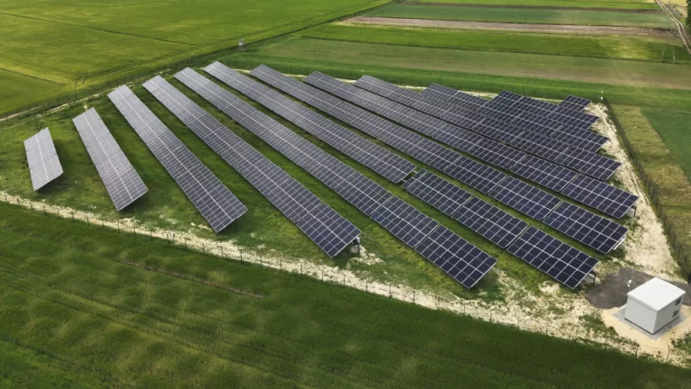 Widok z lotu ptaka na rozległą farmę fotowoltaiczną z panelami ustawionymi na terenie rolniczym, przeznaczoną do generowania energii słonecznej.