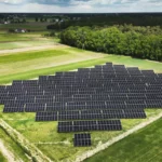 Duża farma fotowoltaiczna z panelami słonecznymi ustawionymi w równych rzędach na polu, otoczona zielonym lasem – produkcja czystej energii odnawialnej.