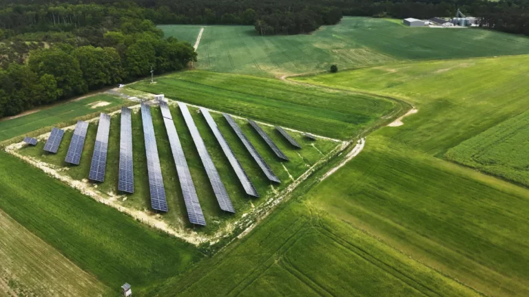 Widok z góry na farmę fotowoltaiczną ulokowaną w pobliżu zabudowań wiejskich – wykorzystanie energii słonecznej w regionie rolniczym.