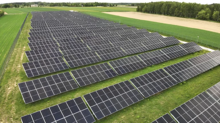 Rzędy paneli fotowoltaicznych zamontowane na szerokim obszarze rolnym, widoczne z góry – inwestycja w energię odnawialną.