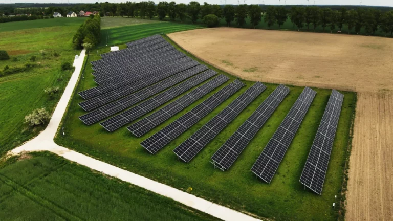 Instalacja fotowoltaiczna zajmująca rozległy teren rolniczy, z widocznymi rzędami paneli słonecznych ułożonych równolegle.