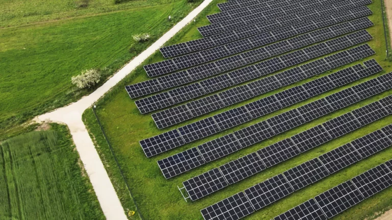 Widok z drona na panele fotowoltaiczne ustawione w równych rzędach w krajobrazie rolniczym – zielona energia przyszłości.